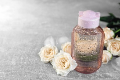 Photo of Micellar water and roses on grey table, closeup. Space for text
