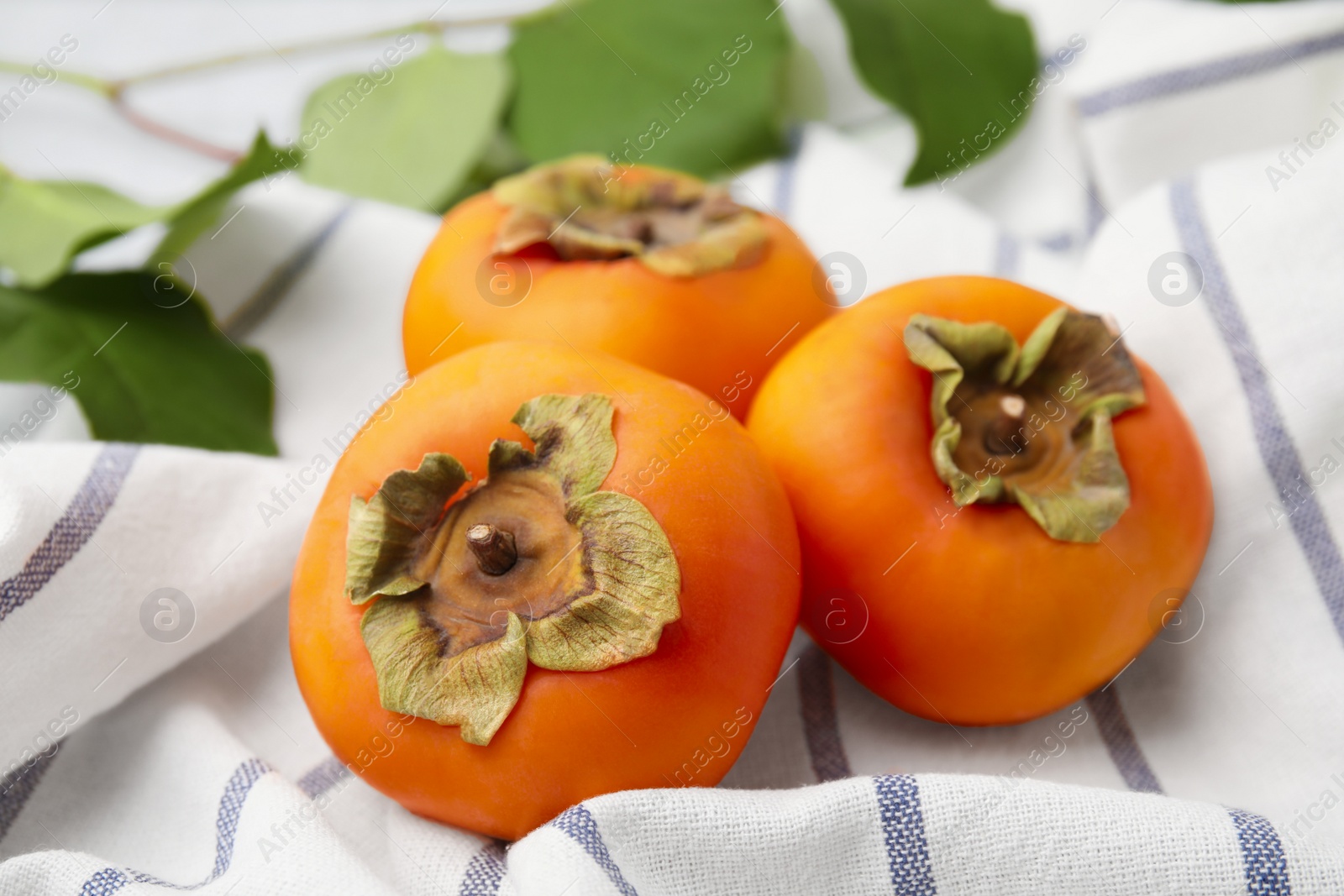 Photo of Delicious ripe juicy persimmons on striped cloth, closeup