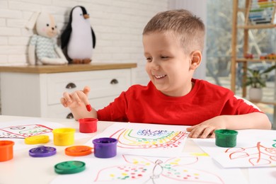 Little boy painting with finger at white table indoors