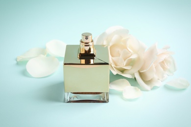 Photo of Bottle of perfume, beautiful roses and petals on light blue background