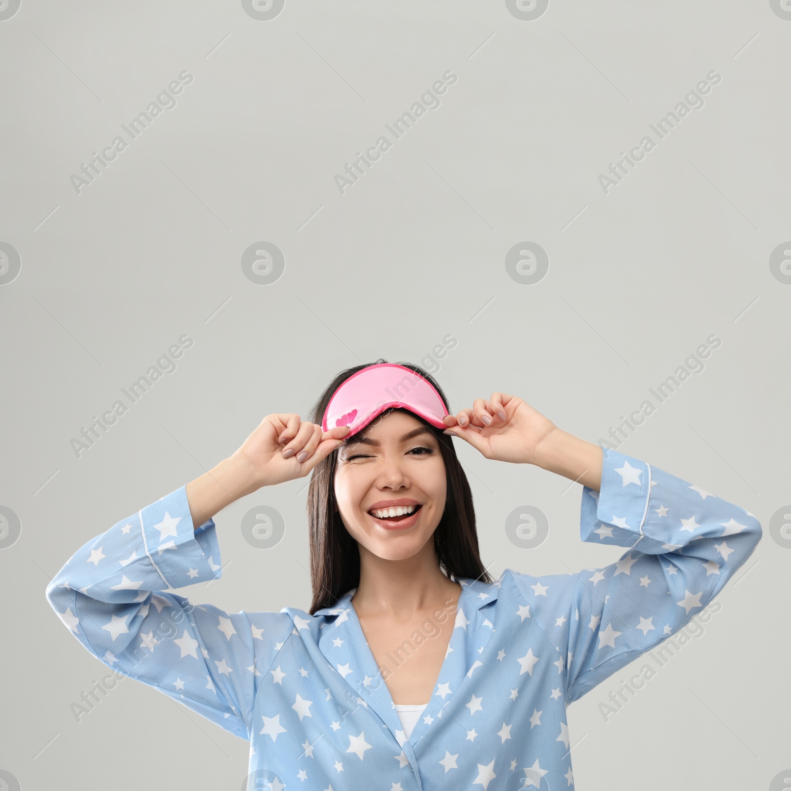 Photo of Beautiful Asian woman wearing pajamas and sleeping mask on light grey background. Bedtime