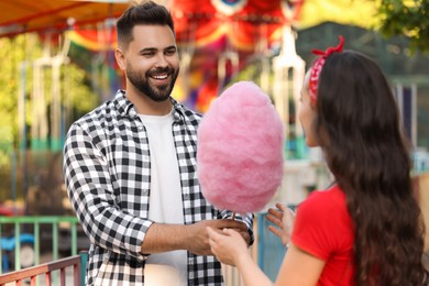 Photo of Happy young man giving his girlfriend cotton candy at funfair