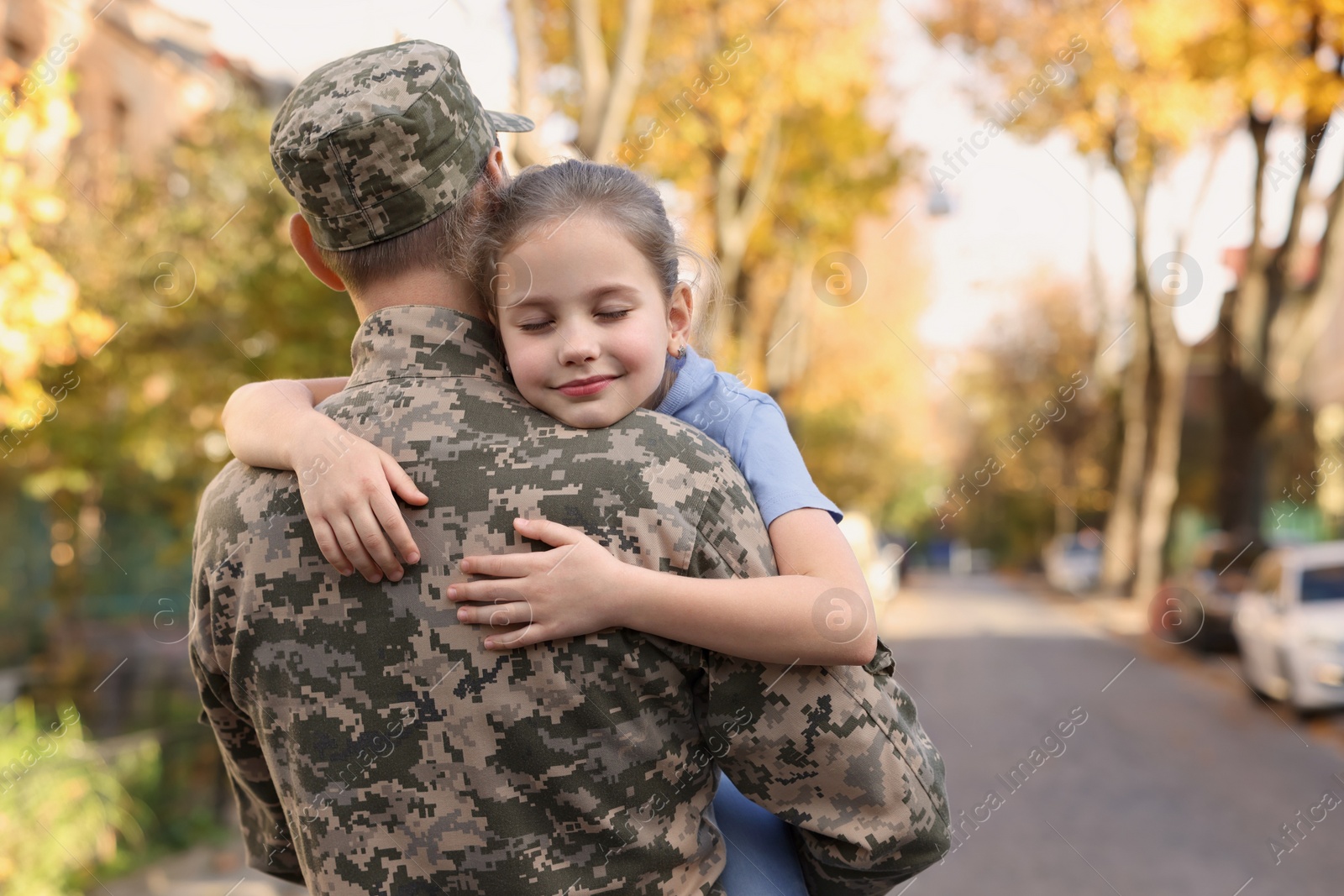 Photo of Daughter hugging her father in Ukrainian military uniform on city street. Family reunion