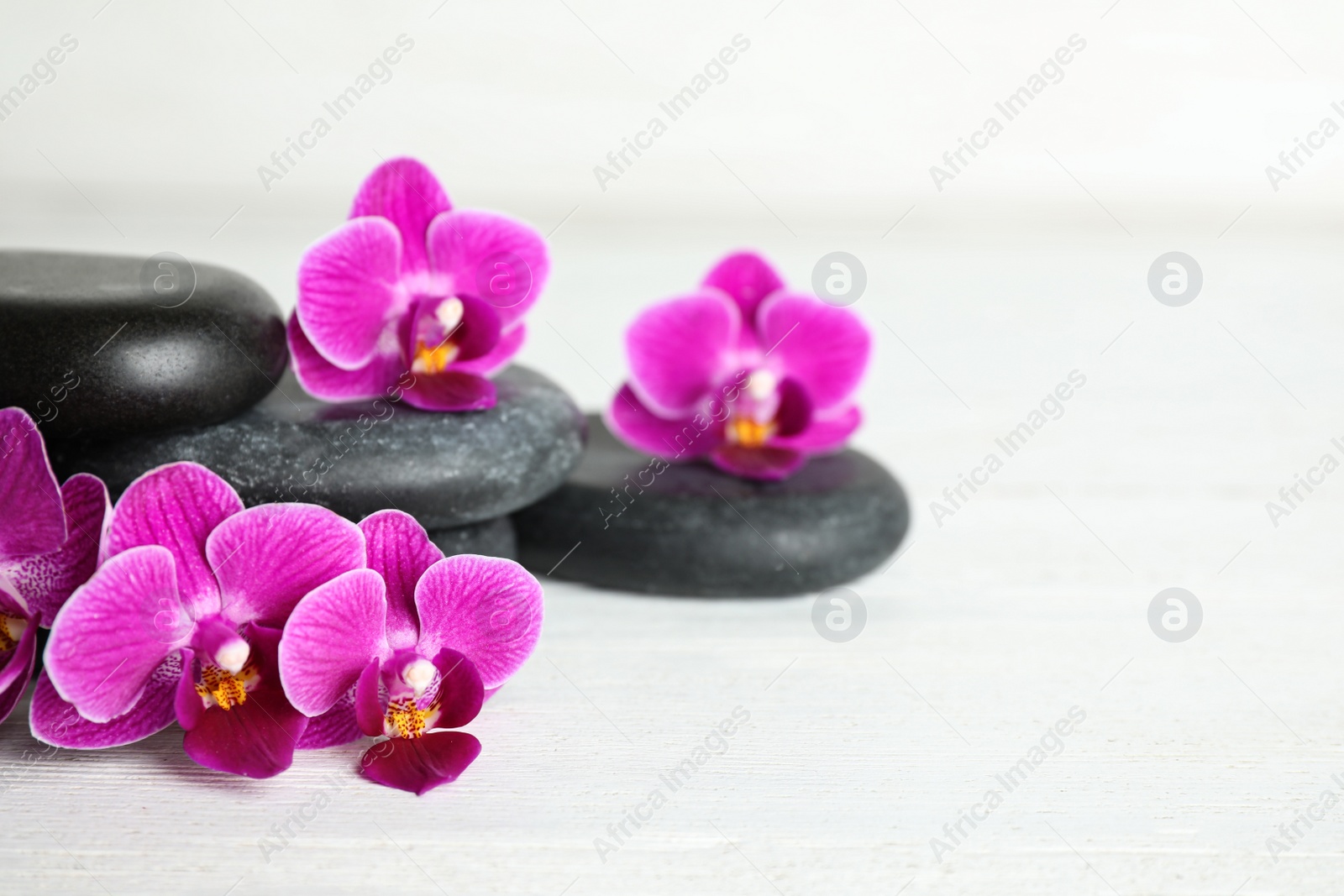 Photo of Spa stones and orchid flowers on white wooden table, space for text