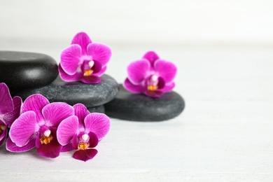 Photo of Spa stones and orchid flowers on white wooden table, space for text