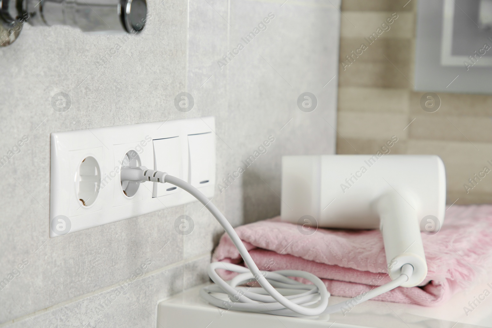 Photo of Hairdryer plugged into power socket on light grey wall, space for text