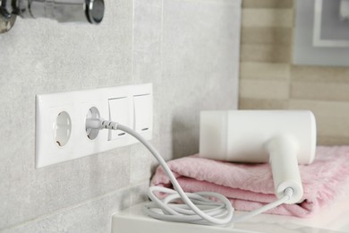 Hairdryer plugged into power socket on light grey wall, space for text