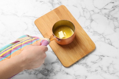 Photo of Woman holding saucepan with melting butter on marble background, closeup