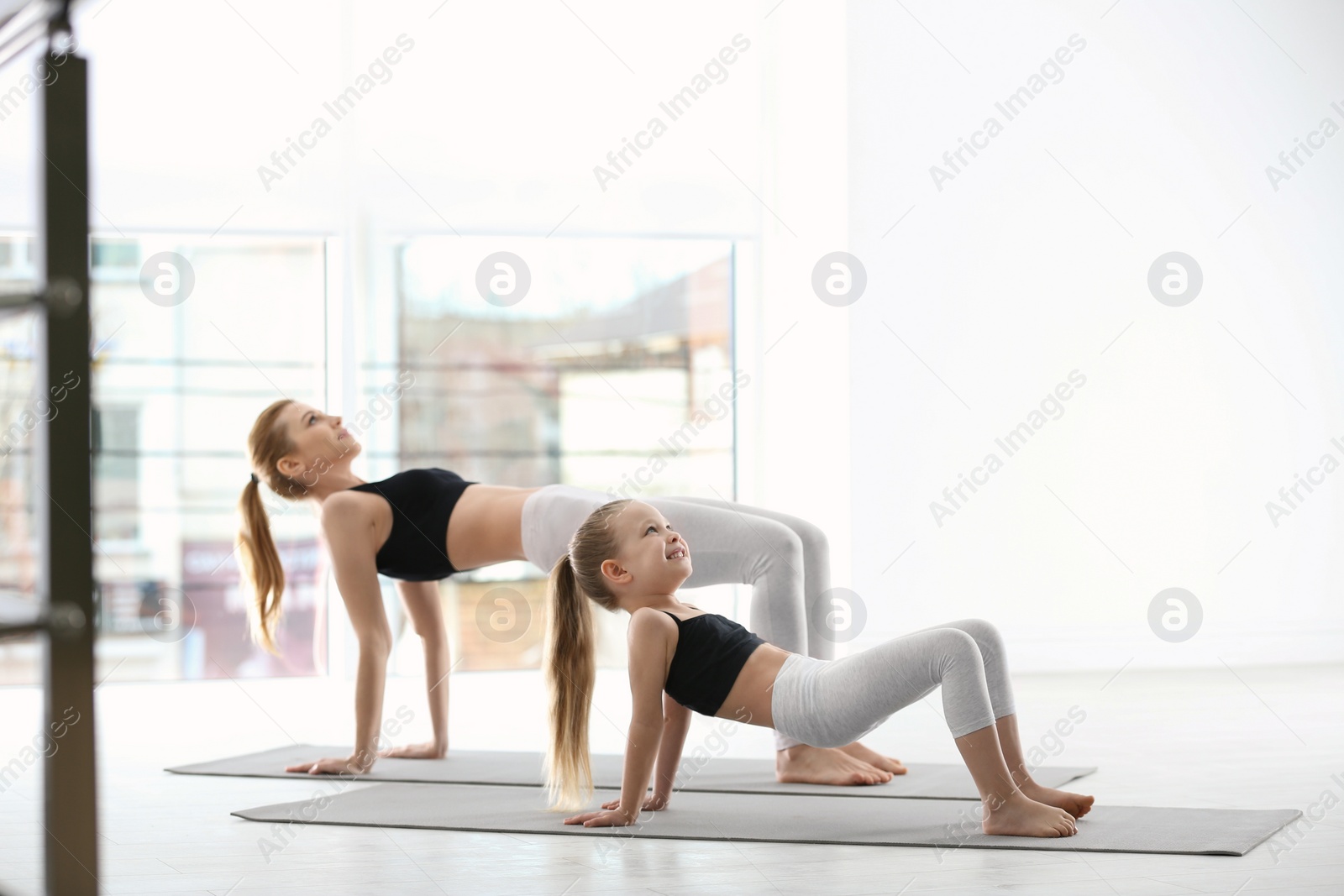 Photo of Mother and daughter in matching sportswear doing yoga together at home