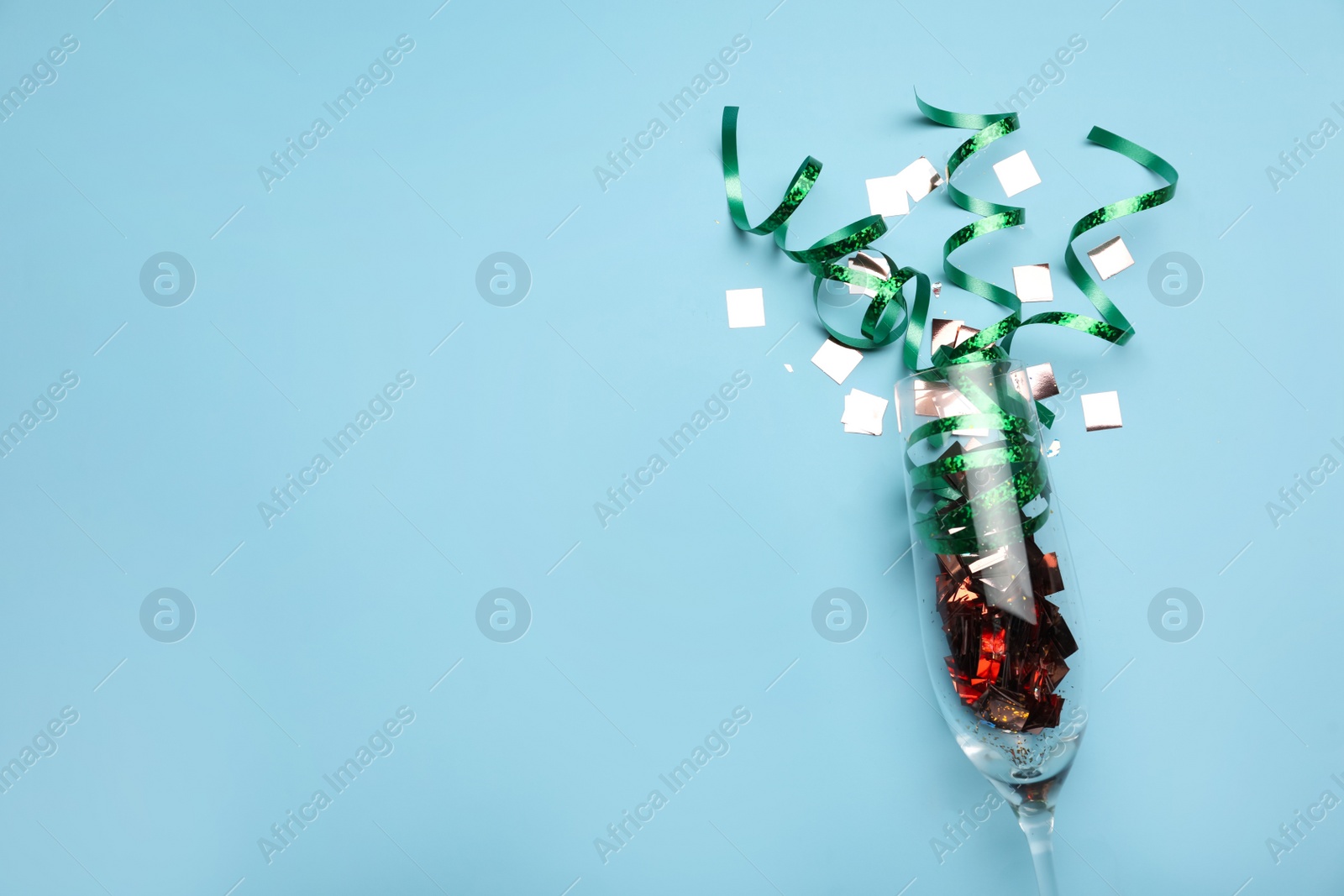 Photo of Flat lay composition with confetti and champagne glass on light blue background. Space for text