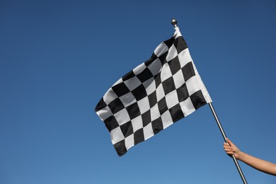 Photo of Woman holding checkered finish flag on light blue background, closeup