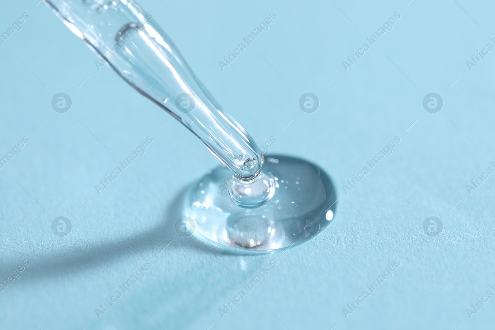 Photo of Glass pipette and transparent liquid on light blue background, closeup