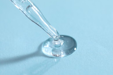 Glass pipette and transparent liquid on light blue background, closeup