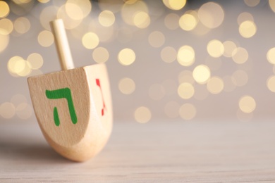 Hanukkah traditional dreidel with letters He and Gimel on wooden table against blurred lights, closeup. Space for text
