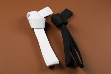 Photo of White and black karate belts on brown background, flat lay