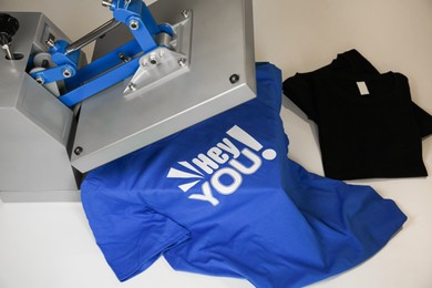 Photo of Printing logo. Heat press with t-shirts on white table