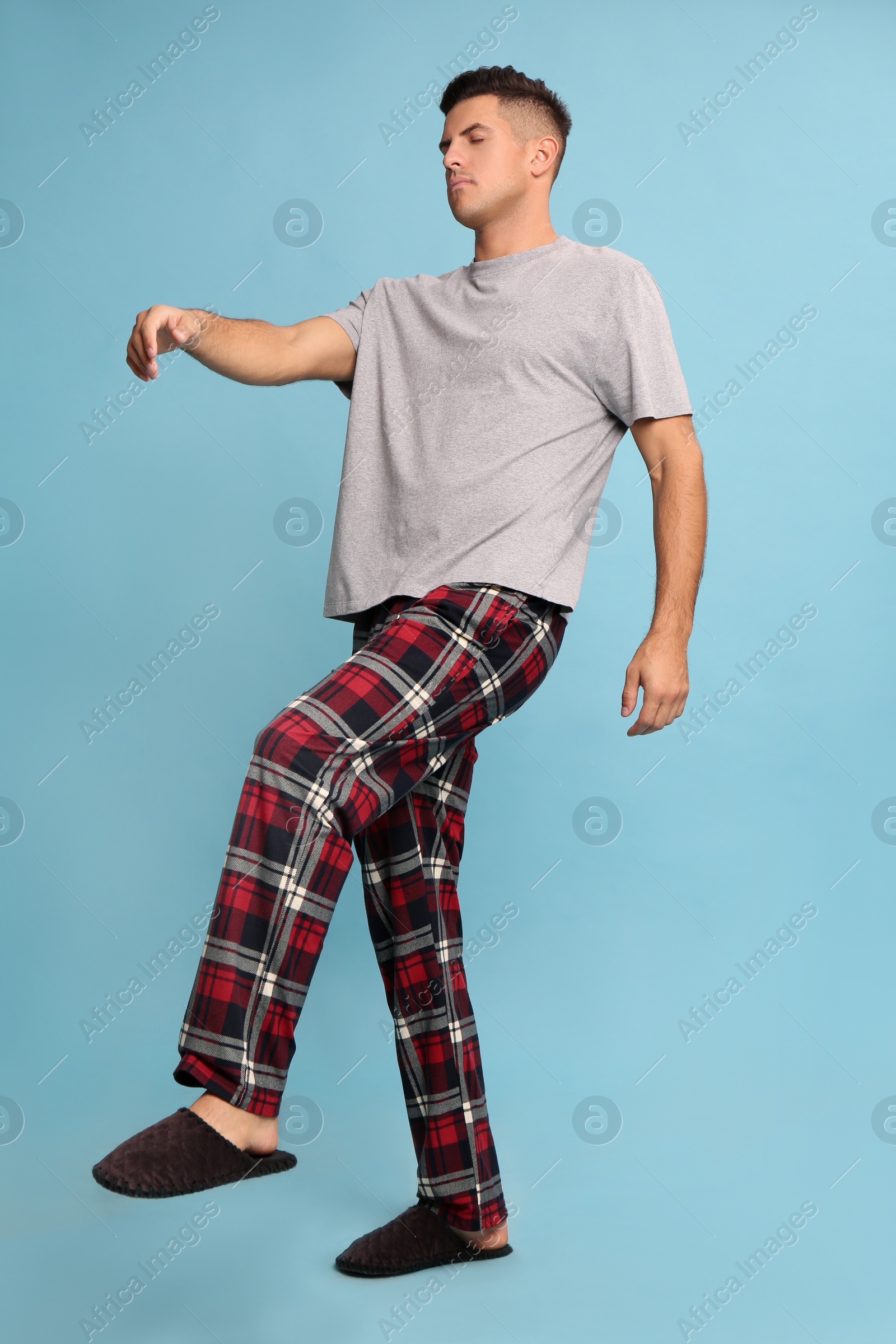 Photo of Somnambulist in pajamas on light blue background. Sleepwalking