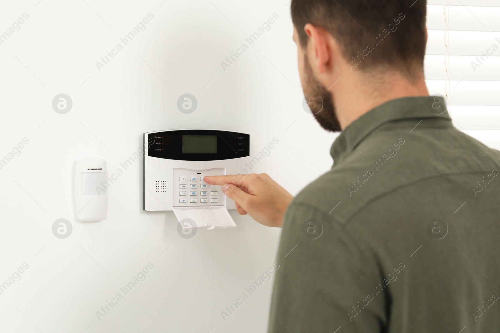 Photo of Man entering code on home security system indoors