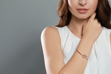 Photo of Young woman wearing elegant bracelet with pearl on grey background, closeup. Space for text