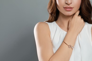 Young woman wearing elegant bracelet with pearl on grey background, closeup. Space for text