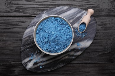 Photo of Bowl and scoop with blue sea salt on dark wooden table, top view