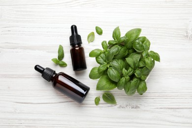 Photo of Glass bottles of basil essential oil and leaves on white  wooden table, flat lay