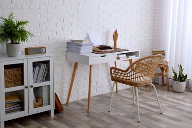 Photo of Comfortable writer's workplace interior with typewriter on desk near white brick wall