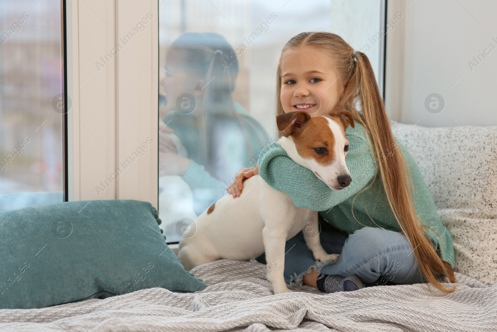 Photo of Cute girl hugging her dog on window sill indoors. Adorable pet