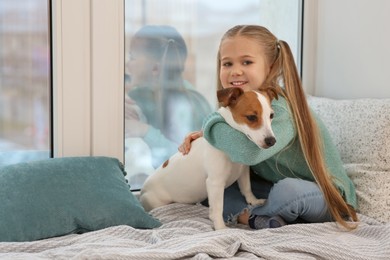 Photo of Cute girl hugging her dog on window sill indoors. Adorable pet