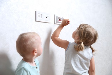 Photo of Little children playing with electrical socket indoors. Dangerous situation
