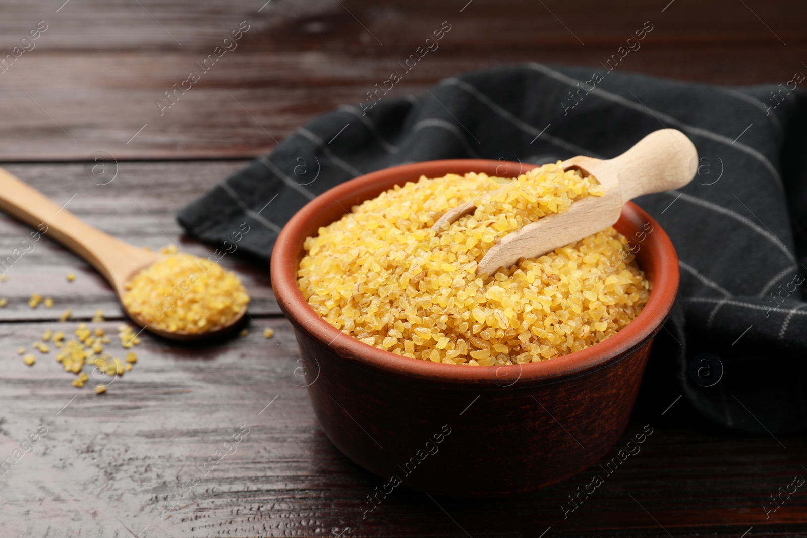 Photo of Bowl and spoon with raw bulgur on wooden table, closeup