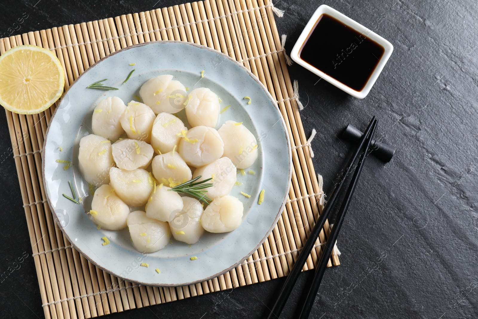 Photo of Raw scallops with lemon, rosemary and soy sauce on dark textured table, flat lay