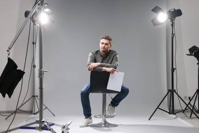 Photo of Casting call. Man with script sitting on chair against grey background in studio