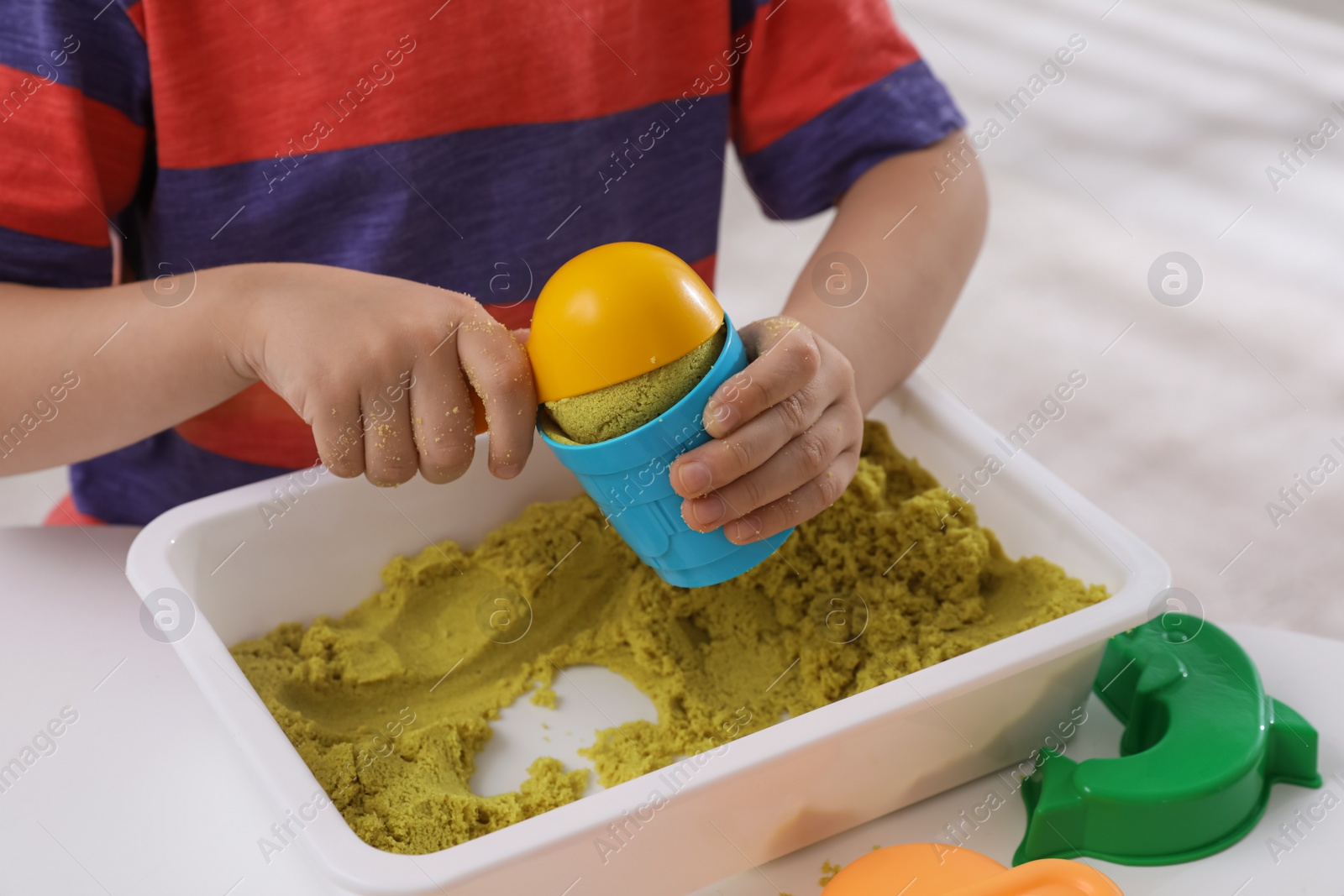 Photo of Little boy playing with bright kinetic sand at table indoors, closeup