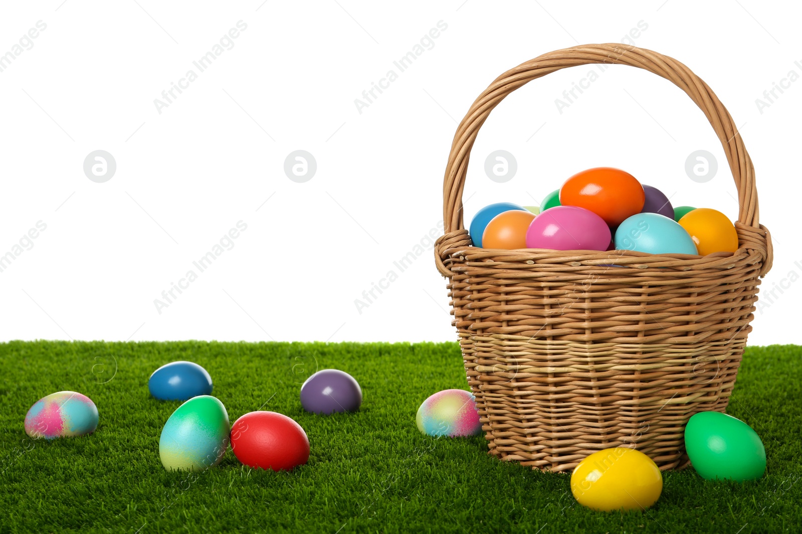 Photo of Wicker basket with bright painted Easter eggs on green grass against white background