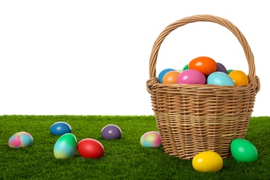 Photo of Wicker basket with bright painted Easter eggs on green grass against white background