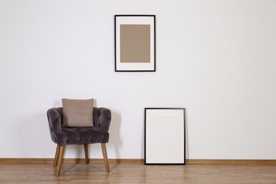 Photo of Comfortable armchair, cushion and frames in room with white wall. Interior design