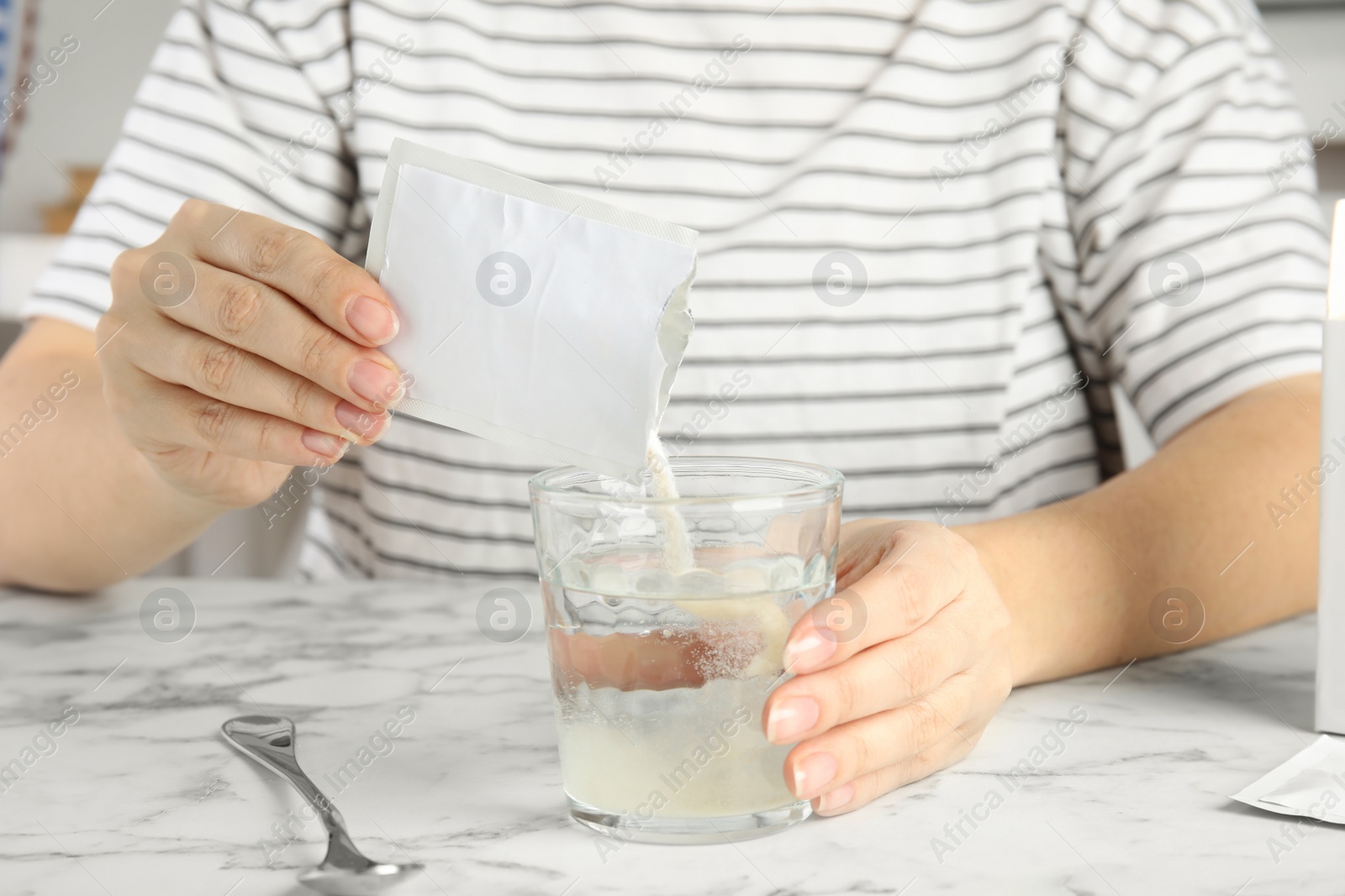 Photo of Woman pouring powder from medicine sachet into glass with water at table, closeup
