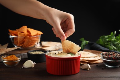 Photo of Woman dipping pita chips into hummus at wooden table, closeup