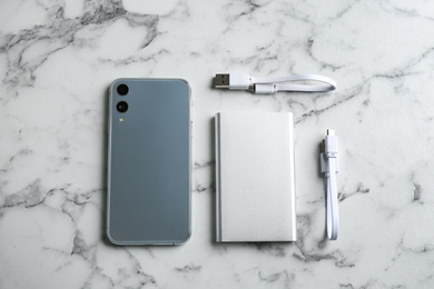 Mobile phone and portable charger on white marble background, flat lay