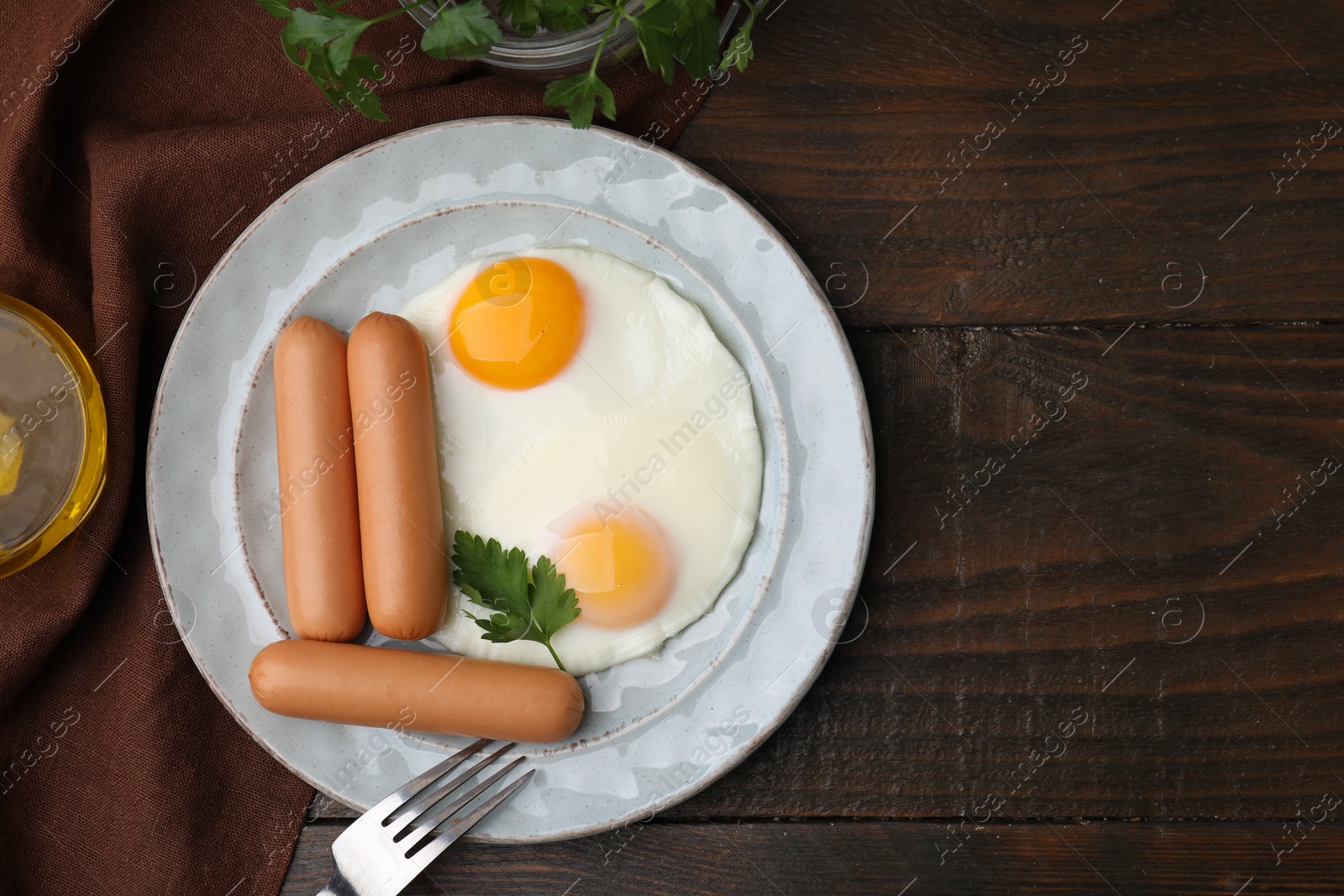 Photo of Delicious boiled sausages and fried eggs served on wooden table, flat lay. Space for text