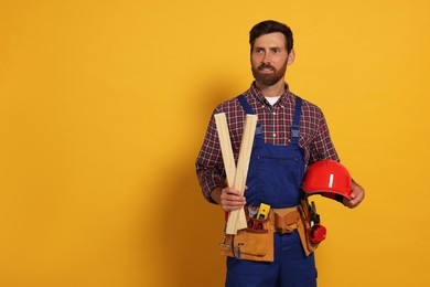 Professional builder in uniform with wooden bars and tool belt on yellow background, space for text