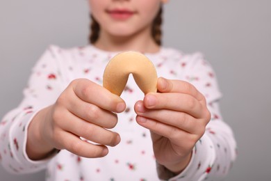 Girl holding tasty fortune cookie with prediction on light grey background, closeup