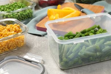Photo of Containers with green beans and fresh products on light gray table, closeup. Food storage