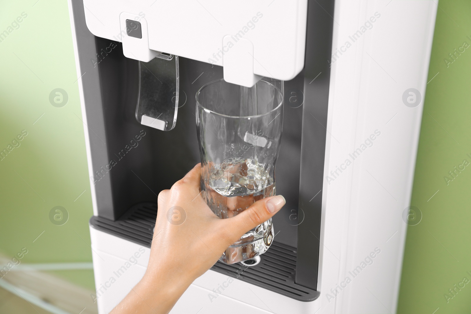 Photo of Woman filling glass from water cooler indoors, closeup. Refreshing drink