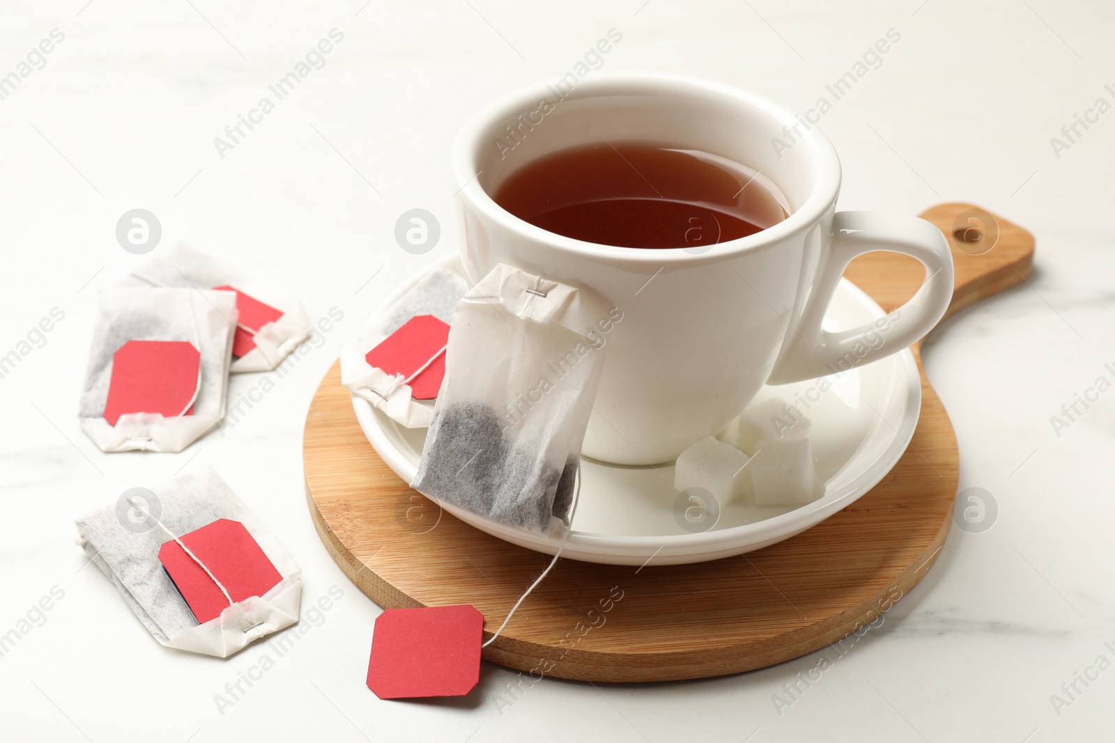 Photo of Tea bags and cup of hot beverage on white table, closeup