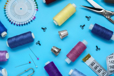 Flat lay composition with thimbles and different sewing tools on light blue background