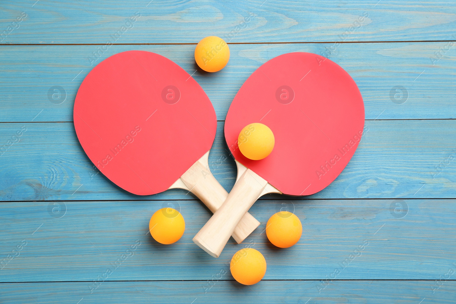 Photo of Ping pong rackets and balls on light blue wooden table, flat lay