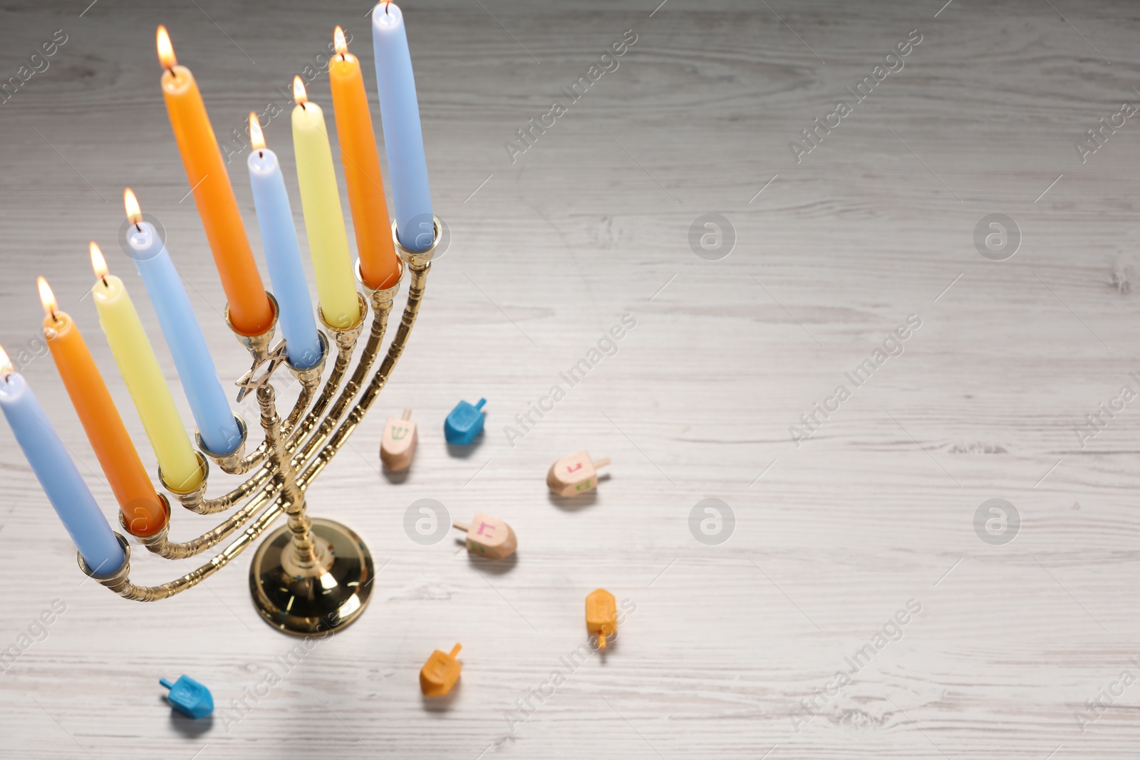 Photo of Hanukkah celebration. Menorah with burning candles and dreidels on light wooden table, above view. Space for text