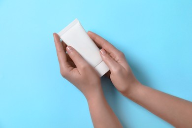 Photo of Woman with tube of hand cream on light blue background, top view